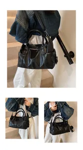 Detail of black leather Boston bag featuring double handles and adjustable shoulder strap