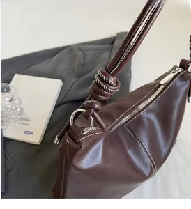 Detailed view of dark brown leather bucket bag with white contrast stitching and silver hardware