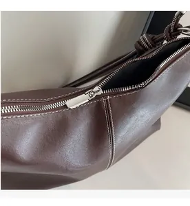 Close-up of smooth silver zipper and white stitching on a dark brown leather bucket bag