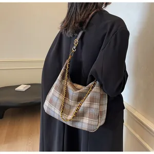 Détail d'un sac à bandoulière à carreaux marron et bleu avec chaîne dorée et cuir