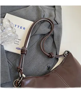 Detail of dark brown bucket bag with white stitching and knotted shoulder strap