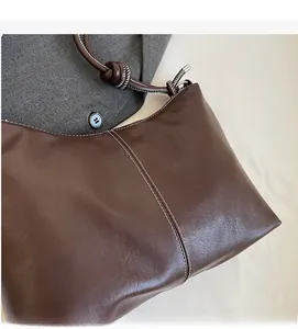 Close-up of retro brown bucket bag with white stitching and silver metal eyelet details