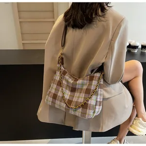 Gros plan d'un sac sous les bras en tweed à carreaux avec chaîne dorée et cuir