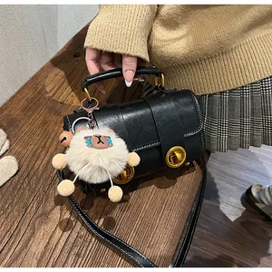 Détail du sac polochon noir avec quincaillerie dorée et breloque en peluche blanche