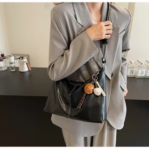 Detail of black leather bucket bag featuring white contrast stitching and baseball charm