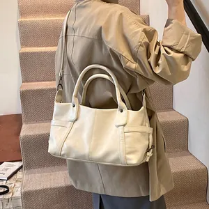 Minimalist beige tote bag in soft synthetic leather worn by a model in a trendy trench coat