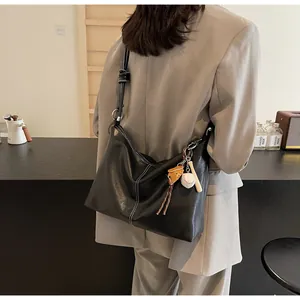 Detail of black leather hobo bag with contrast stitching and baseball charm on model
