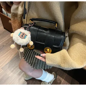 Sac oreiller noir chic avec fermoirs dorés et breloque peluche porté à l'épaule