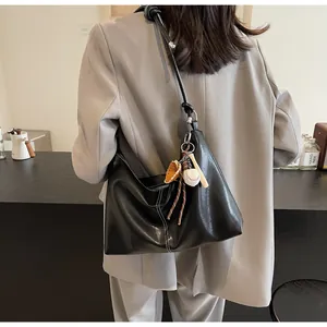 Detail of black hobo bag with contrast stitching and baseball charm on a model's shoulder