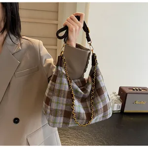 Détail du sac hobo en tweed à carreaux avec chaîne dorée porté sur un blazer beige
