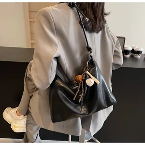 Detail of black PU leather bucket bag featuring knotted shoulder strap and baseball charms