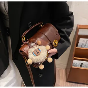 Détail du sac Boston marron foncé avec boucles dorées et breloque mouton en peluche