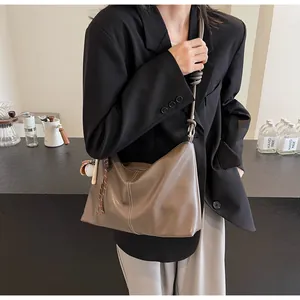 Detail of taupe bucket bag with white stitching, leather knot strap and baseball charm