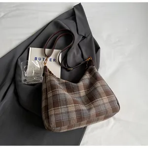Détail du sac à carreaux avec bandoulière en cuir et boucle dorée sur un blazer gris