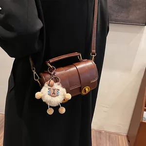 Sac polochon marron rétro avec poignée et breloque peluche porté par un mannequin