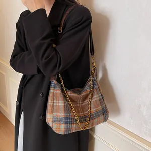 Sac hobo à carreaux classique avec garniture cuir et chaîne dorée sur un manteau noir