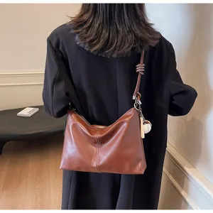 Detail of brown leather bucket bag with baseball charm and vertical white stitching