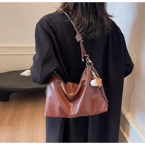 Detail showing brown hobo bag with contrast stitching and baseball charm on a model