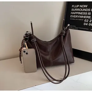 Detail of dark brown leather bucket bag with white stitching and baseball charm beside a phone