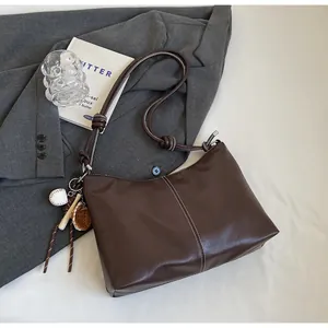 Detail of dark brown bucket bag with contrast stitching and baseball charm on a suit jacket