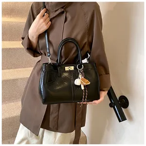 Detail of glossy black leather handbag with silver twist lock and baseball bag charm