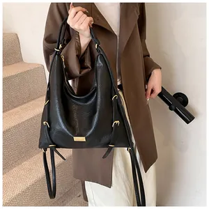 Detail of black leather tote bag featuring gold buckle accents and a metallic logo plate