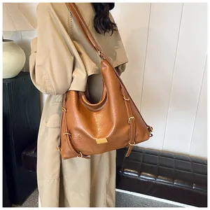 Detail of a brown textured leather tote bag featuring a gold metal logo and hobo style side buckle