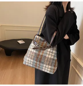 Detail der Vintage-Plaid-Woll-Tragetasche mit gewebter Textur und braunem Lederriemen