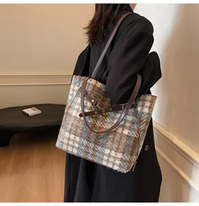 Detail der karierten Tweed-Tragetasche mit goldenen Reißverschlüssen und braunem Trageriemen
