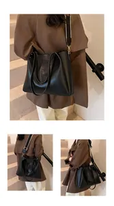 Detail of black tote bag with wide contrast strap and logo embossing on matte PU leather