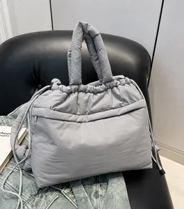 Detail view of the grey puffer tote bag with drawstring straps on a leather sofa