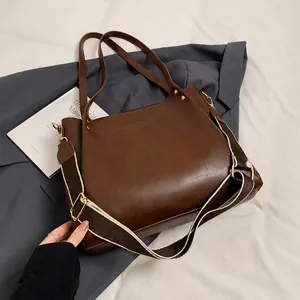 Close-up of brown matte leather tote bag with wide woven strap and gold metal hardware
