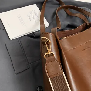 Detail of golden metal hook and brown leather strap on a large tote bag with brand embossing