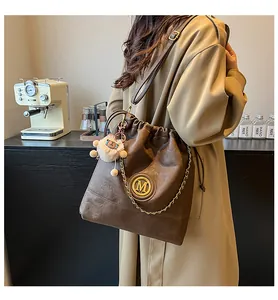 Détail du sac seau en cuir marron avec logo M doré chaîne et breloque ours en peluche