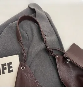 Detail of dark brown tote bag showing knotted strap, white stitching, and metal eyelets