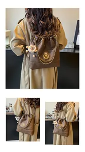 Détail d'un sac à dos en cuir marron avec logo M doré et porte-clés mouton en peluche blanc