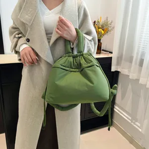 Quilted grass green puffer tote bag with drawstring closure shown on a model in wool coat