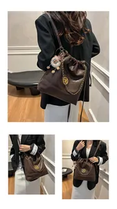 Détail du sac seau marron foncé avec logo M doré, chaîne et breloque ours en peluche