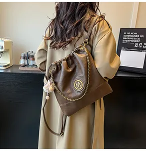 Détail d'un cabas marron foncé à cordon avec logo M en métal et pompon sur bandoulière chaîne