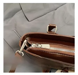 Detailed close-up of polished silver hardware and branded zipper on dark brown leather tote