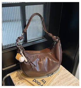Detail of dark brown crescent bag with white contrast stitching and baseball charm
