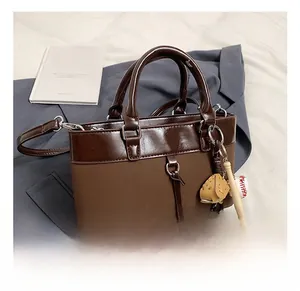 Detail of dark brown leather tote bag showing buckle closure and baseball glove charm