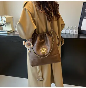 Détail du sac seau en cuir marron foncé avec logo M doré et pendentif ours mignon