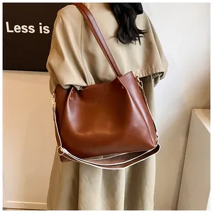 Brown leather tote bag paired with stylish trench coat and wide woven shoulder strap