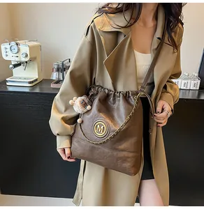 Détail d'un sac à bandoulière en cuir marron avec logo M doré et chaîne métallique