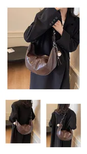Close-up of dark brown crescent bag with white stitching and baseball charm detail