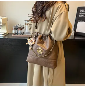 Détail du sac seau marron foncé avec logo M doré et breloque lion en peluche
