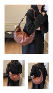 Detail of caramel leather croissant bag with knotted strap and baseball charm