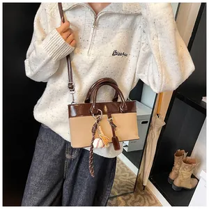 Detail view of stylish two-tone tote bag with baseball charm on a beige sweater