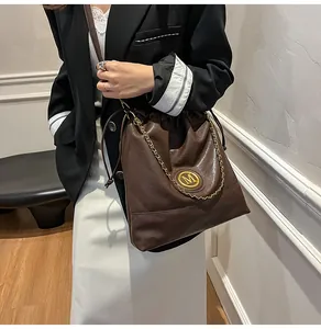 Détail d'un sac seau en cuir marron foncé avec logo M doré et décor de chaîne